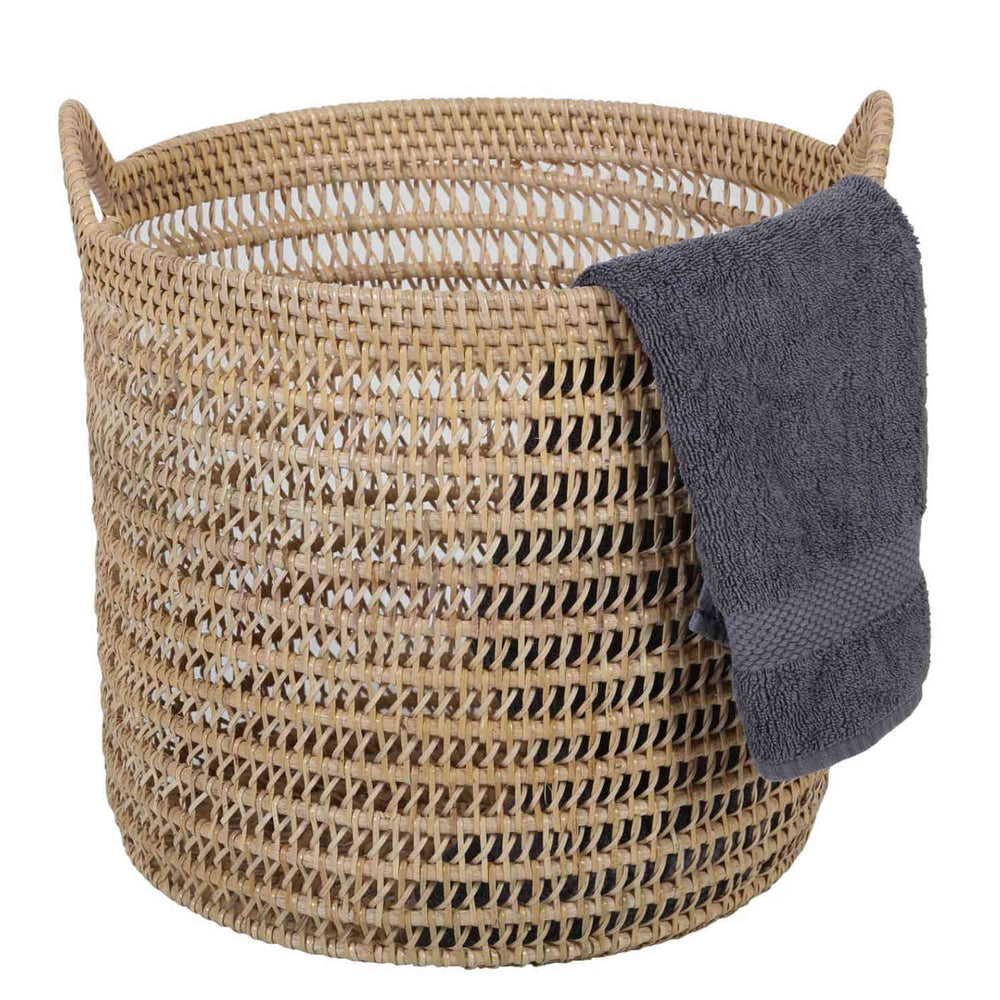 Natural-coloured Eda rattan basket with an open weave, two handles and a dark grey towel over the rim.