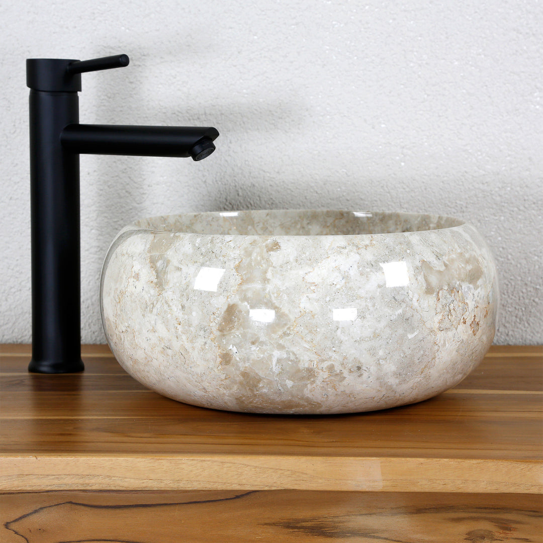 Round countertop basin made of light natural stone on a wooden top with a black fitting in a neutral studio setting