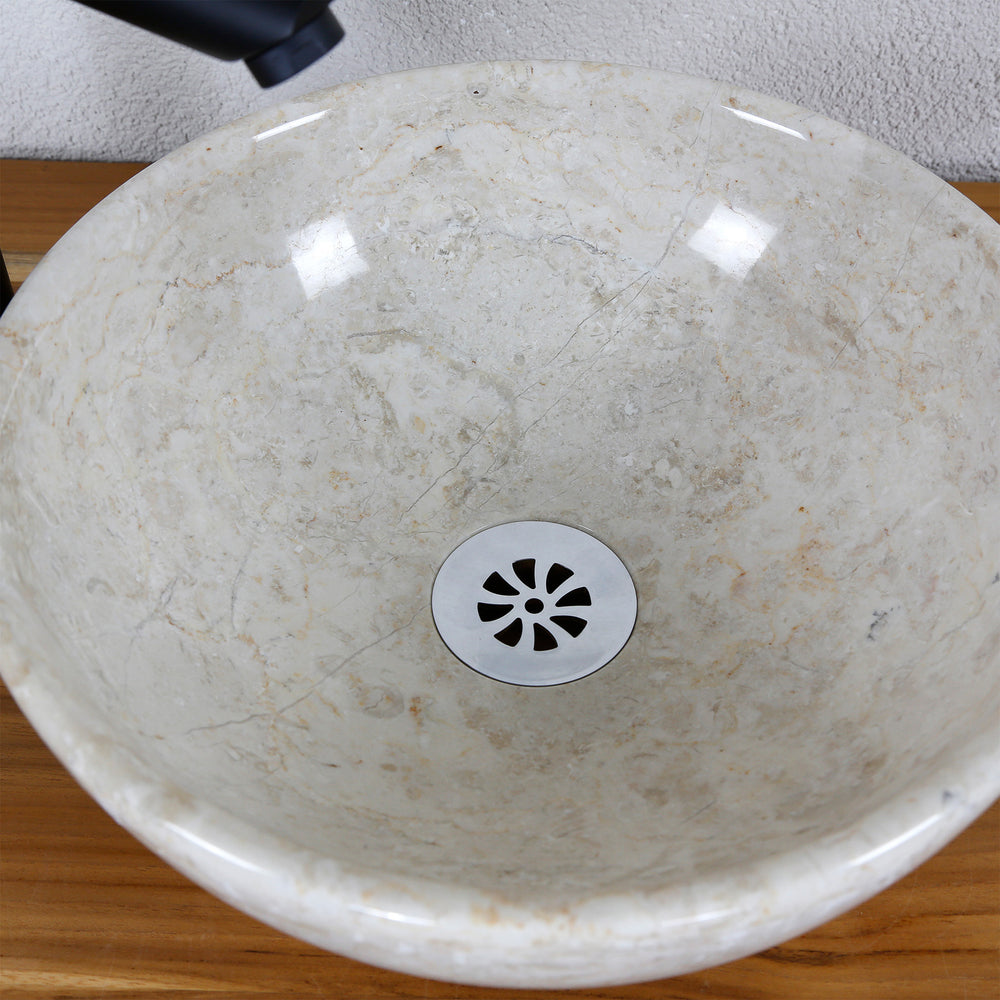Detailed view of a round countertop basin made of light natural stone with a polished inner surface and a central drain