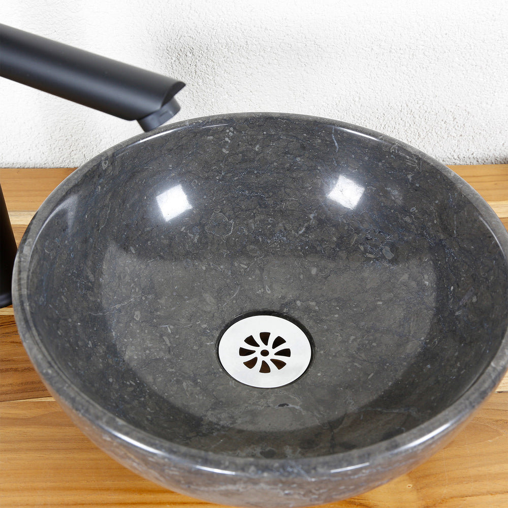 Round countertop washbasin made of natural stone in detail with polished inner surface, stainless steel drain and fitting