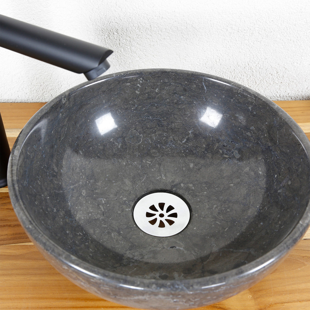 Round countertop washbasin made of natural stone in detail with polished inner surface, stainless steel drain and fitting