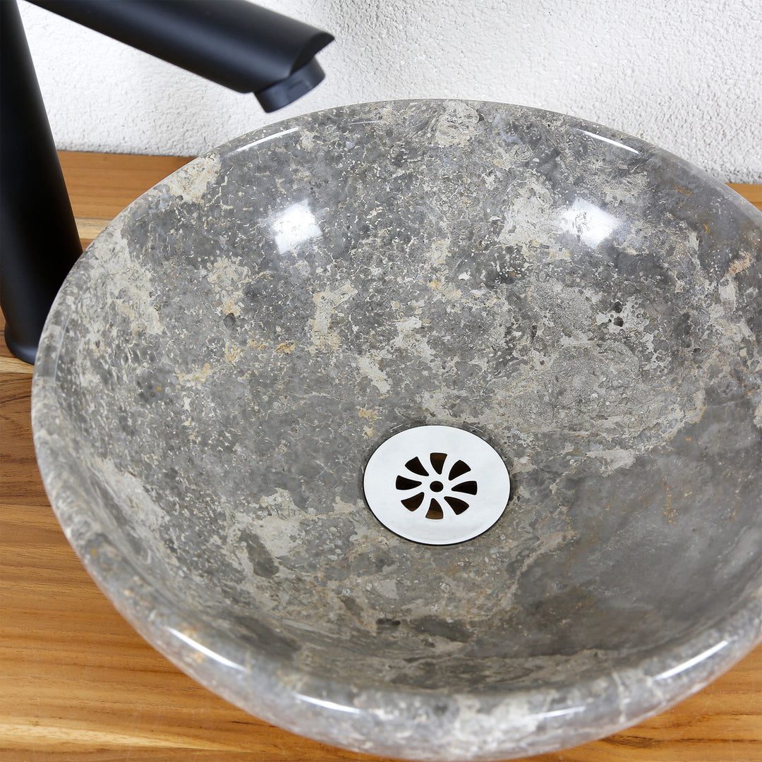 View of the natural stone countertop washbasin with gray-brown grain and stainless steel drain cover, combined with a black stand-alone tap