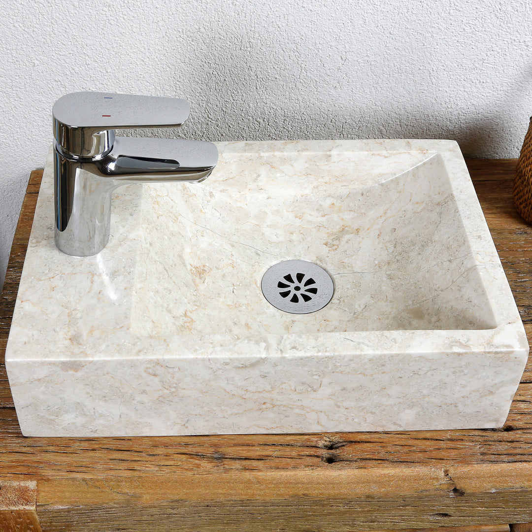 Square countertop washbasin made of light stone with straight edges and central drain on a wooden top