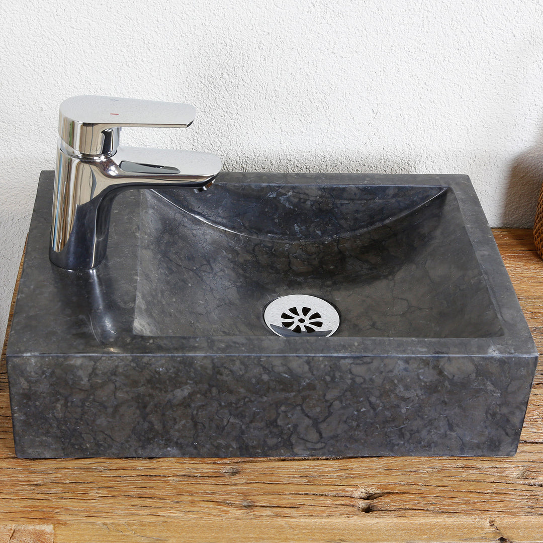 Square stone sink with dark marble grain on wooden top, with chrome-plated tap and stainless steel drain cover
