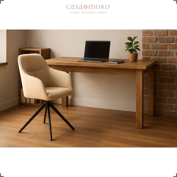 360° rotating upholstered chair with armrests in beige at a wooden table with a laptop, modern workstation in the home office with warm light and a brick wall