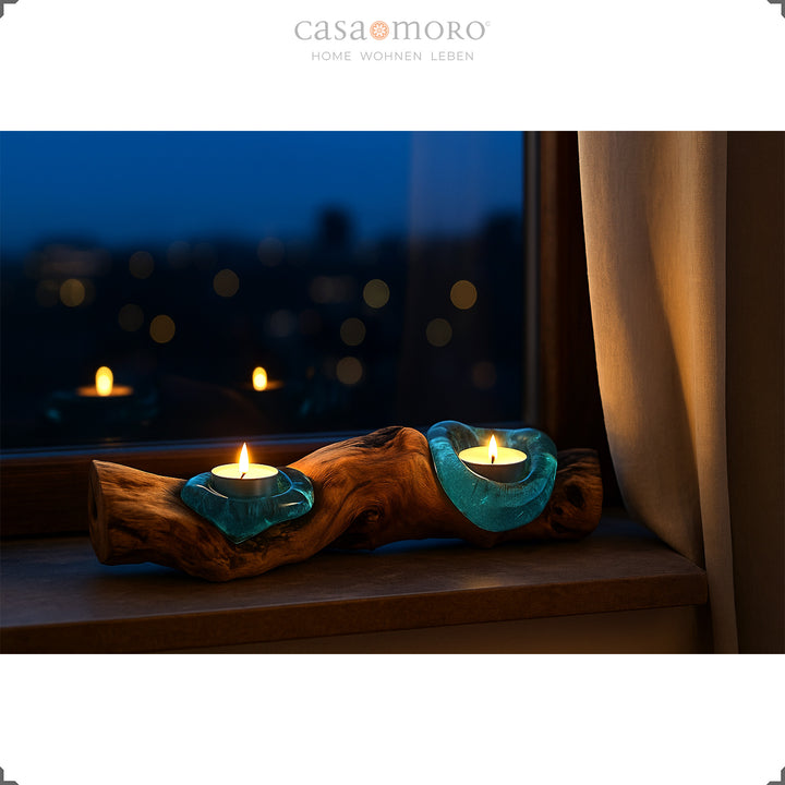 Elongated tea light holder made of glass and root wood on a windowsill, its warm light glows gently into the evening atmosphere.