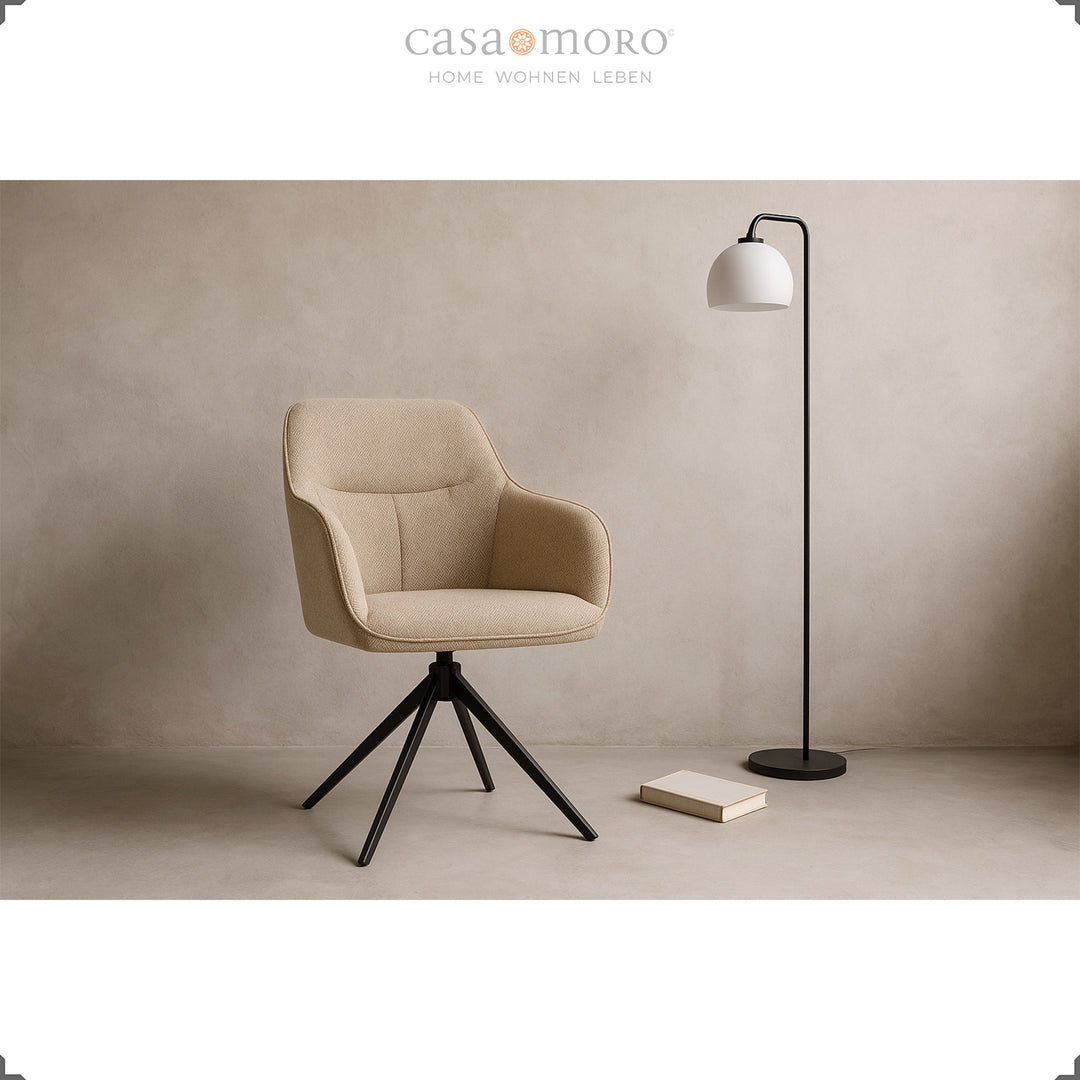 Modern 360° rotating upholstered chair with armrests in beige, staged in the living room with a black floor lamp and book on a light floor