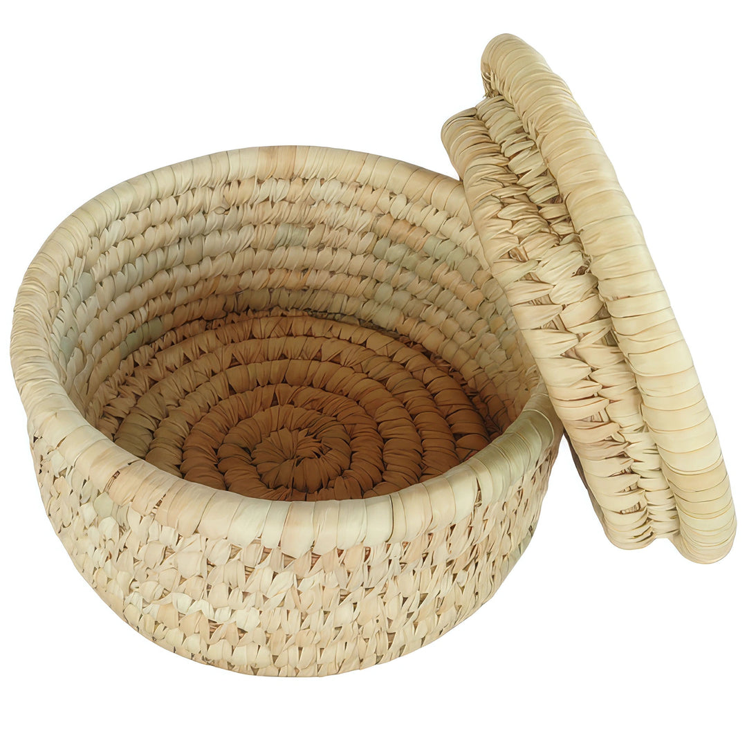 Open round palm leaf basket in natural tones, visible woven inner base and spiral-pattern lid leaning on the right.