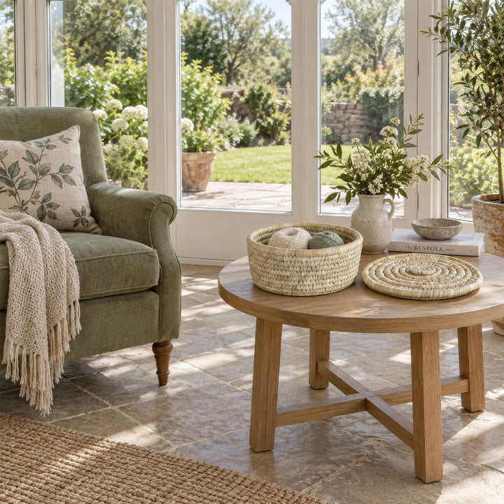 An open palm-leaf basket, 28 cm in diameter, containing balls of wool and with its lid set aside, sitting on a table in the sunroom.