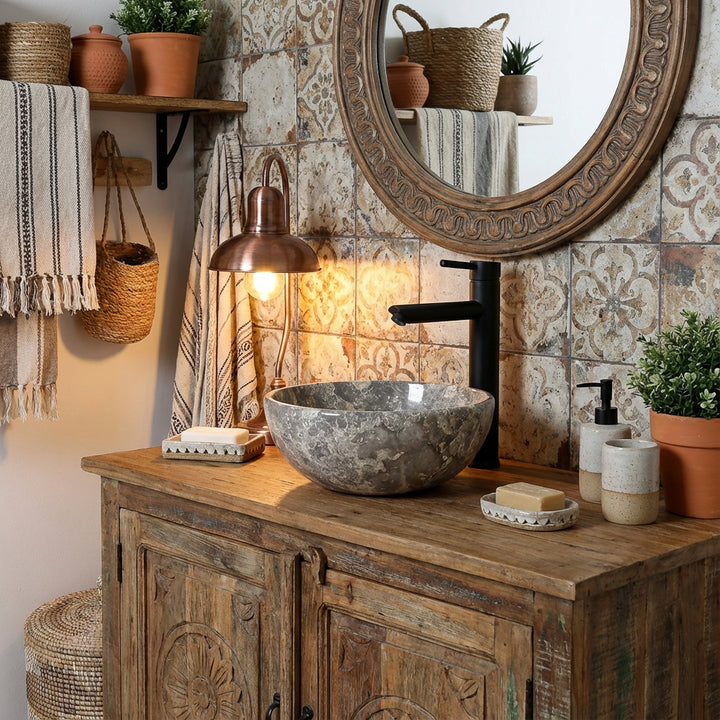 Round marble countertop washbasin with gray grain on rustic wooden washstand in cozy bathroom, combined with black fittings, patterned tiles and warm lighting