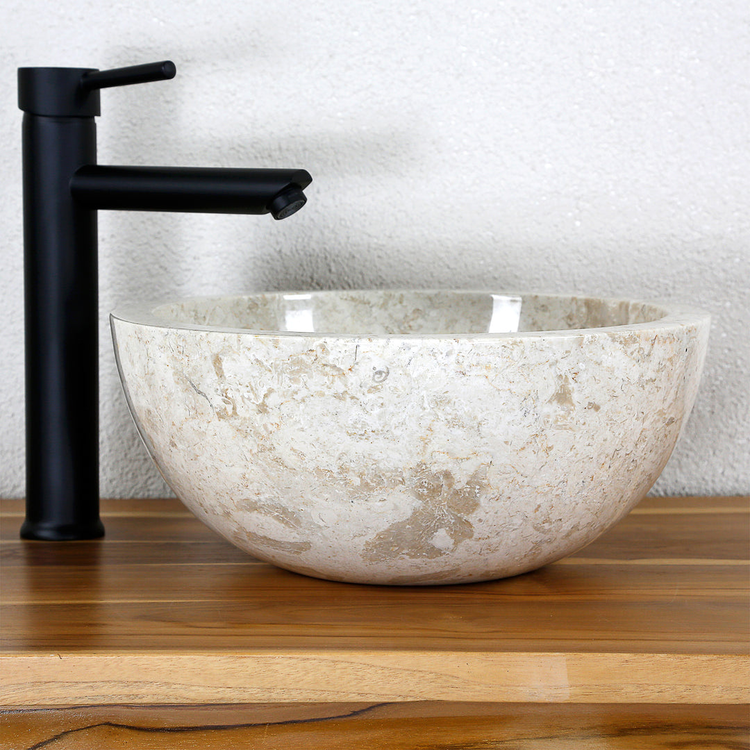 Round countertop basin made of light natural stone on a wooden top with a black fitting in a simple studio setting