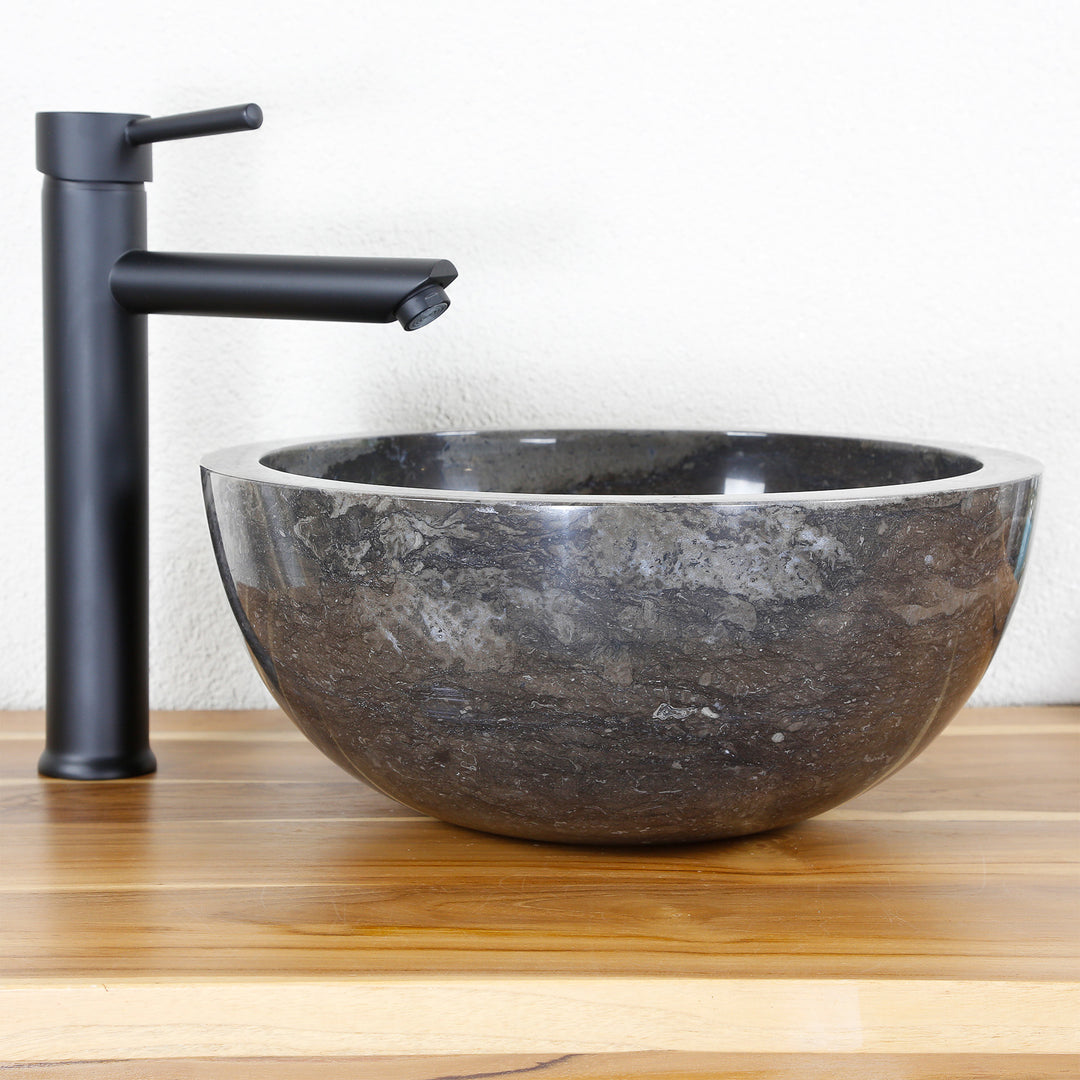 Round stone washbasin made of dark natural material as an attachment on a wooden top with a black fitting, clean studio setting