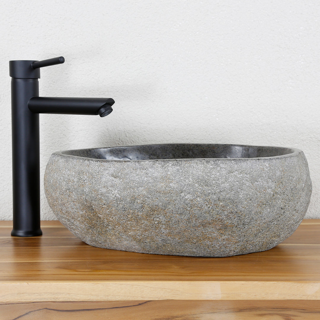 Washbasin Made of gray natural stone in an oval shape, combined with black fittings on a warm wooden top