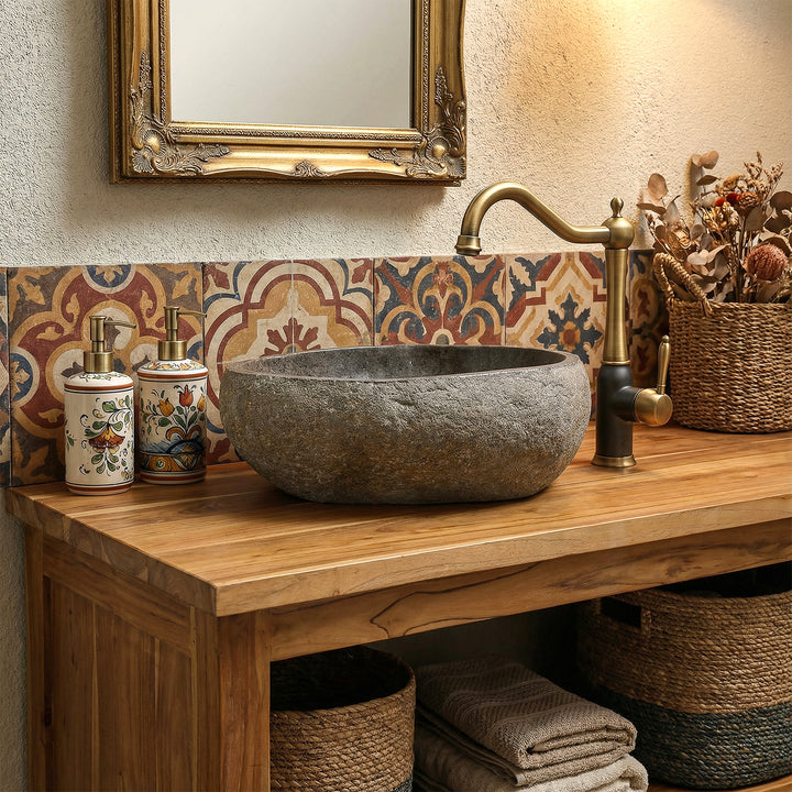 Natural stone sink in warm boho bathroom on wooden vanity unit, combined with brass fittings and patterned tiles