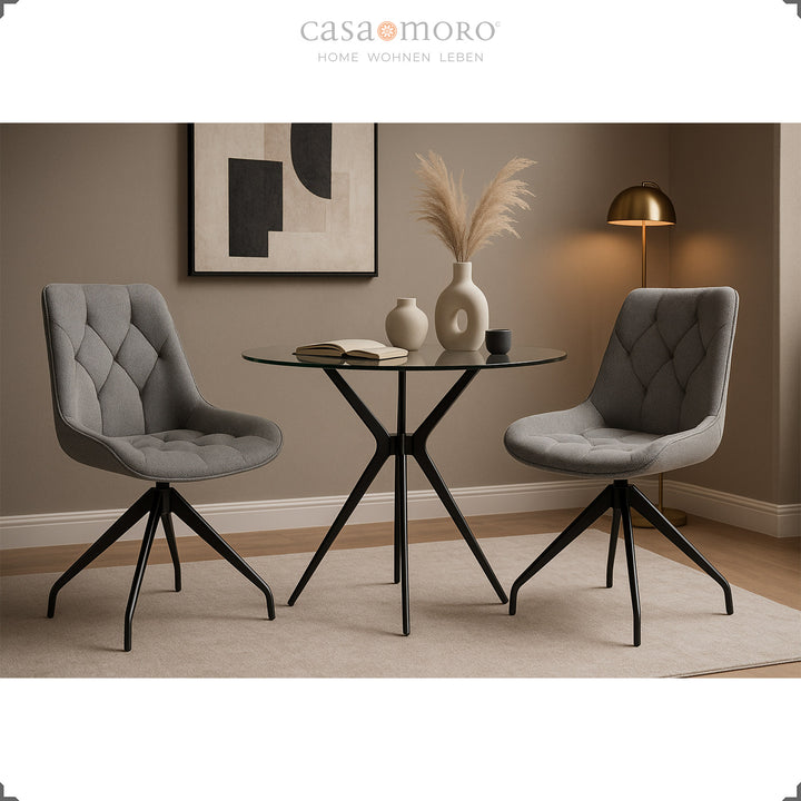 Two gray dining chairs with 360° swivel function and black metal frame - stylish seating area with glass table and warm lighting ambience