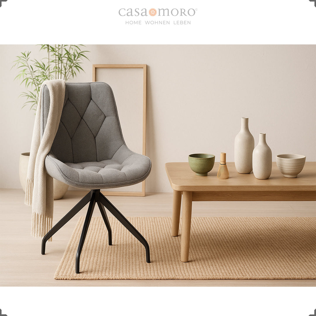 Gray upholstered chair with 360° swivel function and black metal frame - modern accent chair next to wooden table with ceramic decoration in a natural living ambience