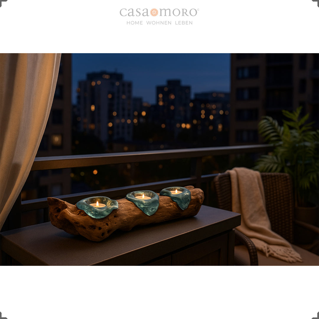 Three-part tea light holder made of glass and burl wood on a balcony at night, with a city view and a comfortable seat