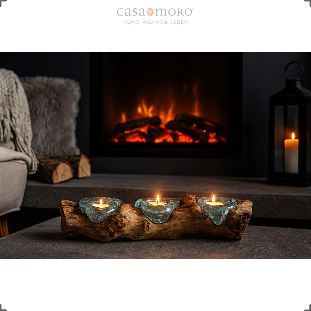 Three-part tea light holder made of glass and burl wood in front of a fireplace, glowing warmly in the cozy living room