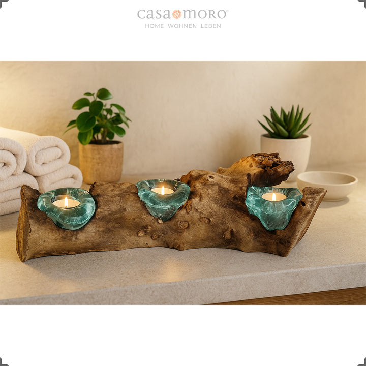 Three-piece tea light holder made of burl wood and turquoise glass on a bathroom shelf, surrounded by plants and towels