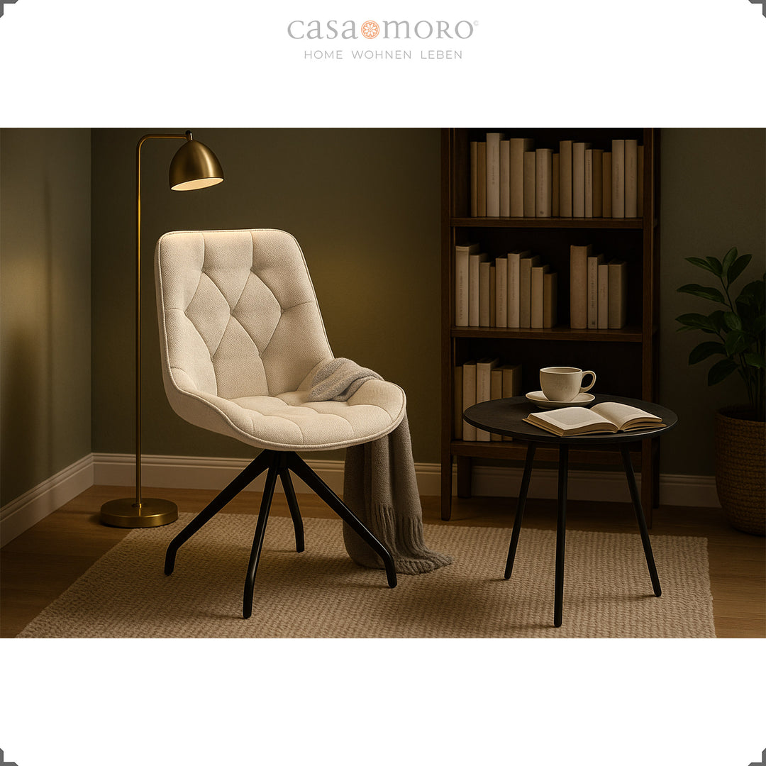 Upholstered chair that can be rotated 360° in beige with a black metal frame - cozy reading corner with side table, bookshelf and floor lamp in warm light