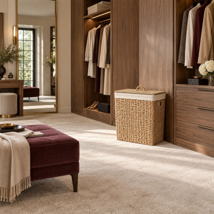A rectangular seagrass laundry basket with a lid and a 90-liter capacity, placed in front of a wooden cabinet in the dressing room.