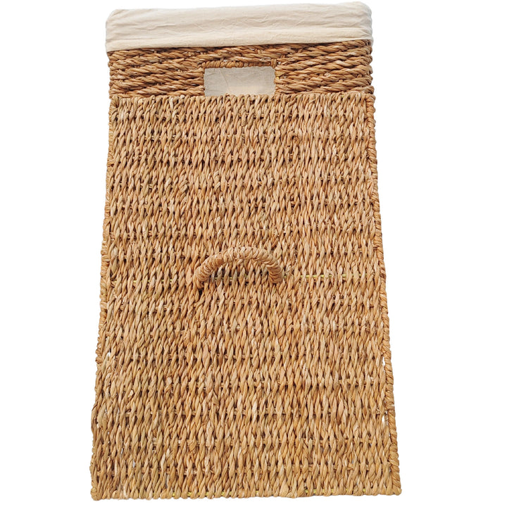 Rectangular laundry basket made of seagrass with a 90-liter capacity, a light-colored fabric liner, and a lid that rests against the front with a handle.