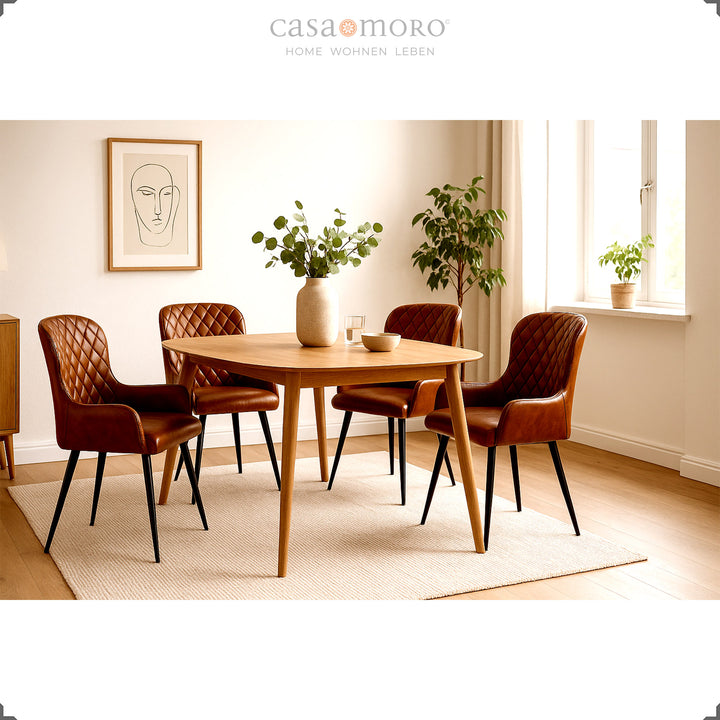 Four antique brown leather chairs with diamond quilting around a round wooden table in a bright, friendly living room with plants and natural light.